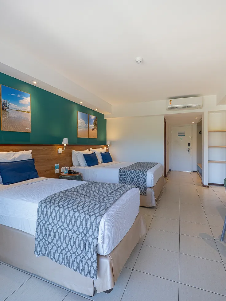Apartamento Standard no Salinas Maceió com duas camas, uma de casal e outra de solteiro, decoração praiana com parede verde e quadros pendurados, ambiente amplo e confortável.