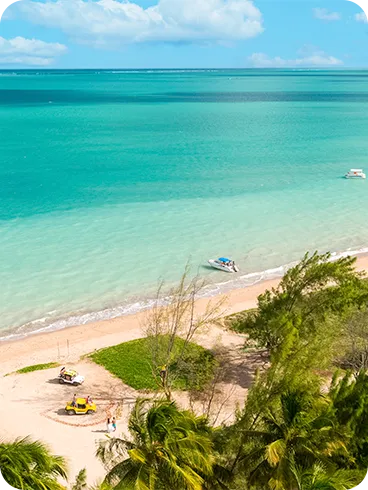 Vista aérea da Praia de Burgalhau com mar turquesa em degradê, coqueiros, barcos espalhados e faixa de areia clara com alguns buggys.