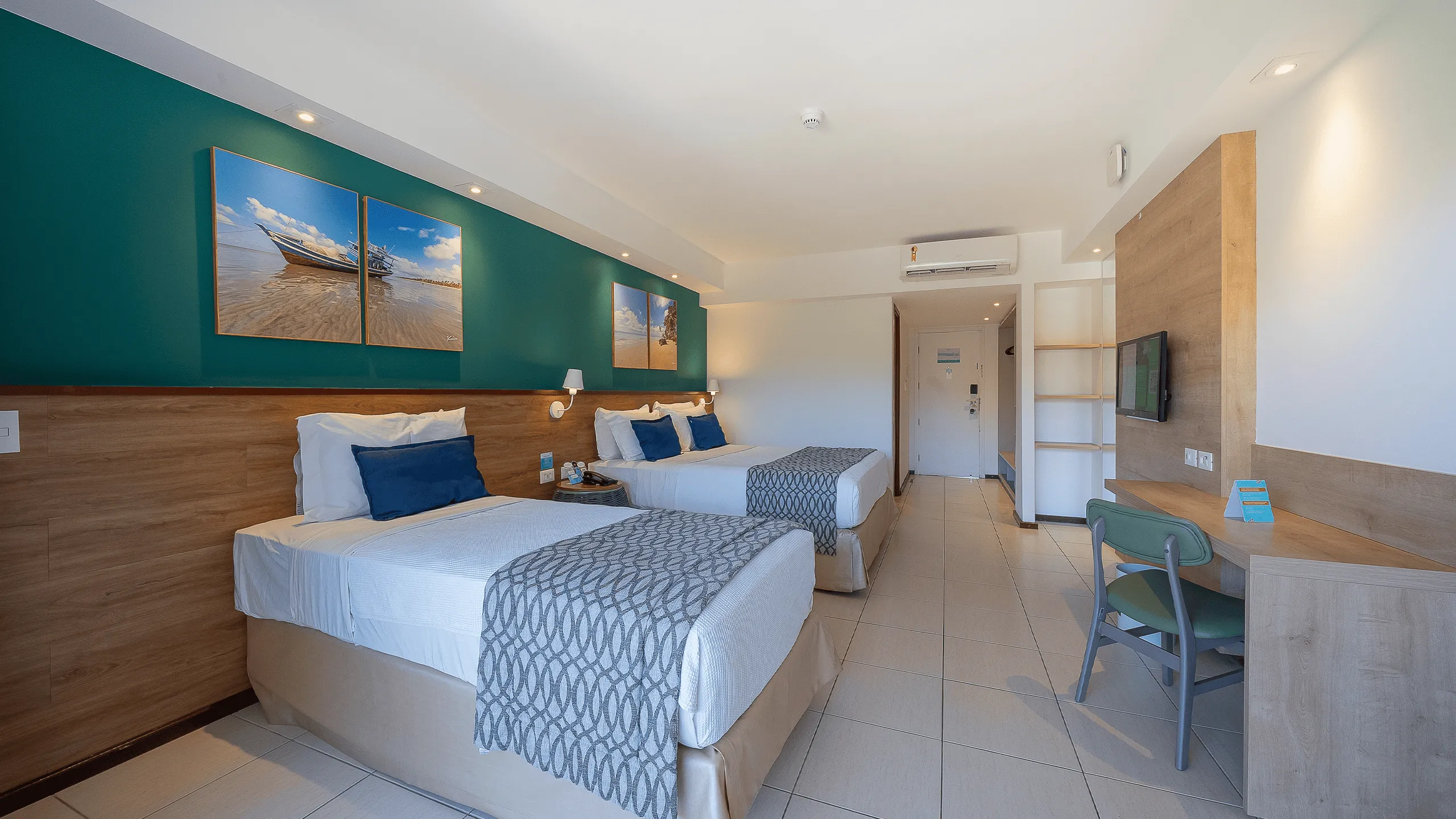 Apartamento Standard no Salinas Maceió com duas camas, uma de casal e outra de solteiro, decoração praiana com parede verde e quadros pendurados, ambiente amplo e confortável.