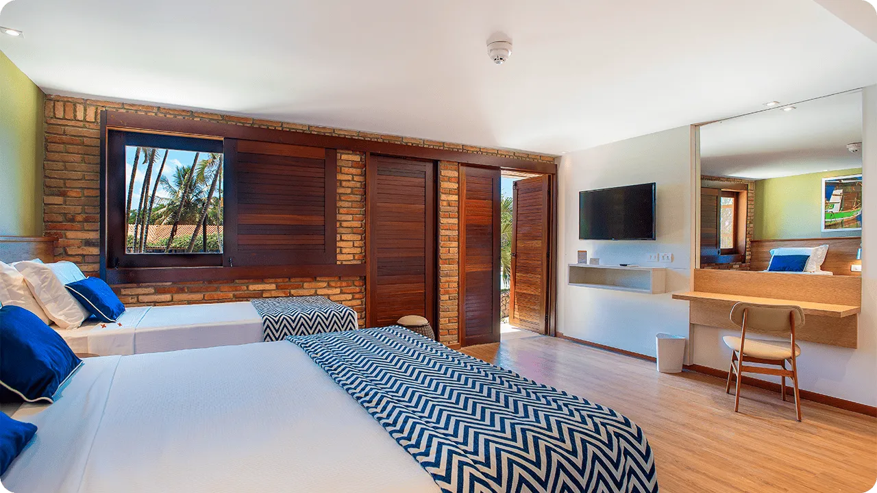 Parte de la Suite Familia, uno de los alojamientos en Salinas Maragogi, con una cama queen y una cama individual, lámparas, un marco decorativo de madera con fotografías de las playas de Maragogi y una pared de ladrillo.