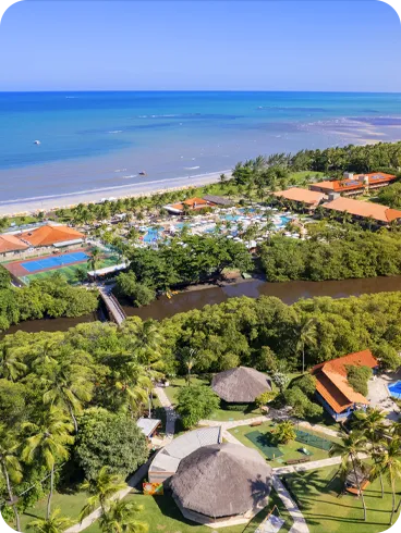Vista aérea panorámica del resort Salinas Maragogi, que muestra su ubicación privilegiada entre el mar y el río Maragogi. La imagen muestra los edificios del hotel, el parque acuático, los puentes que cruzan el río y la densa vegetación circundante.
