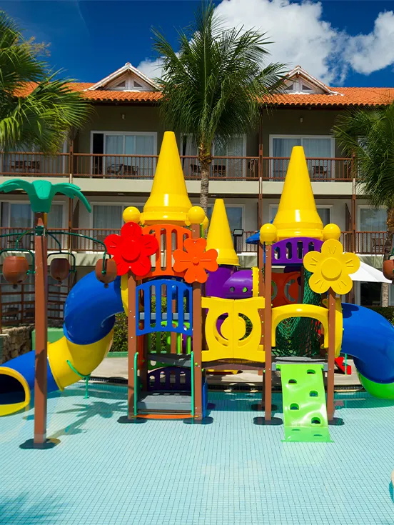 Brinquedão infantil na piscina infantil do Salinas Maceió. Ao fundo os apartamentos do resort com varandas, alguns coqueiros e área de lazer.
