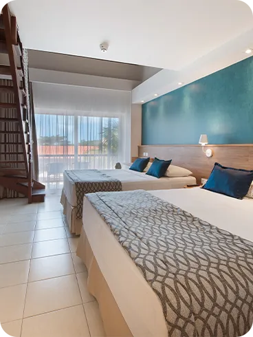 Ground floor of the Family Suite room with a mezzanine. Two queen-size beds, two lamps, one for each bed, wood paneling with cable TV, mirror, closet, and stairs leading to the first floor.