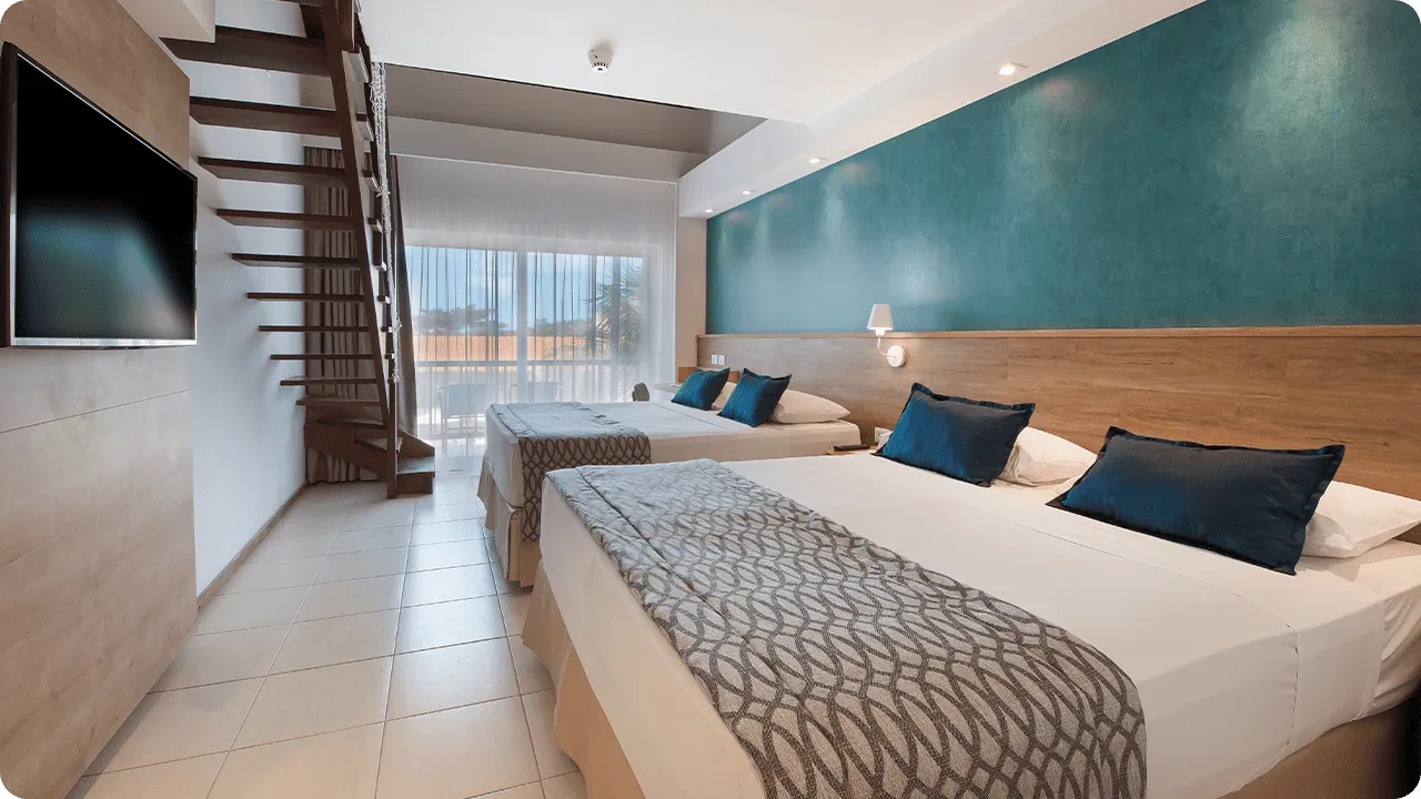 Ground floor of the Family Suite room with a mezzanine. Two queen-size beds, two lamps, one for each bed, wood paneling with cable TV, mirror, closet, and stairs leading to the first floor.