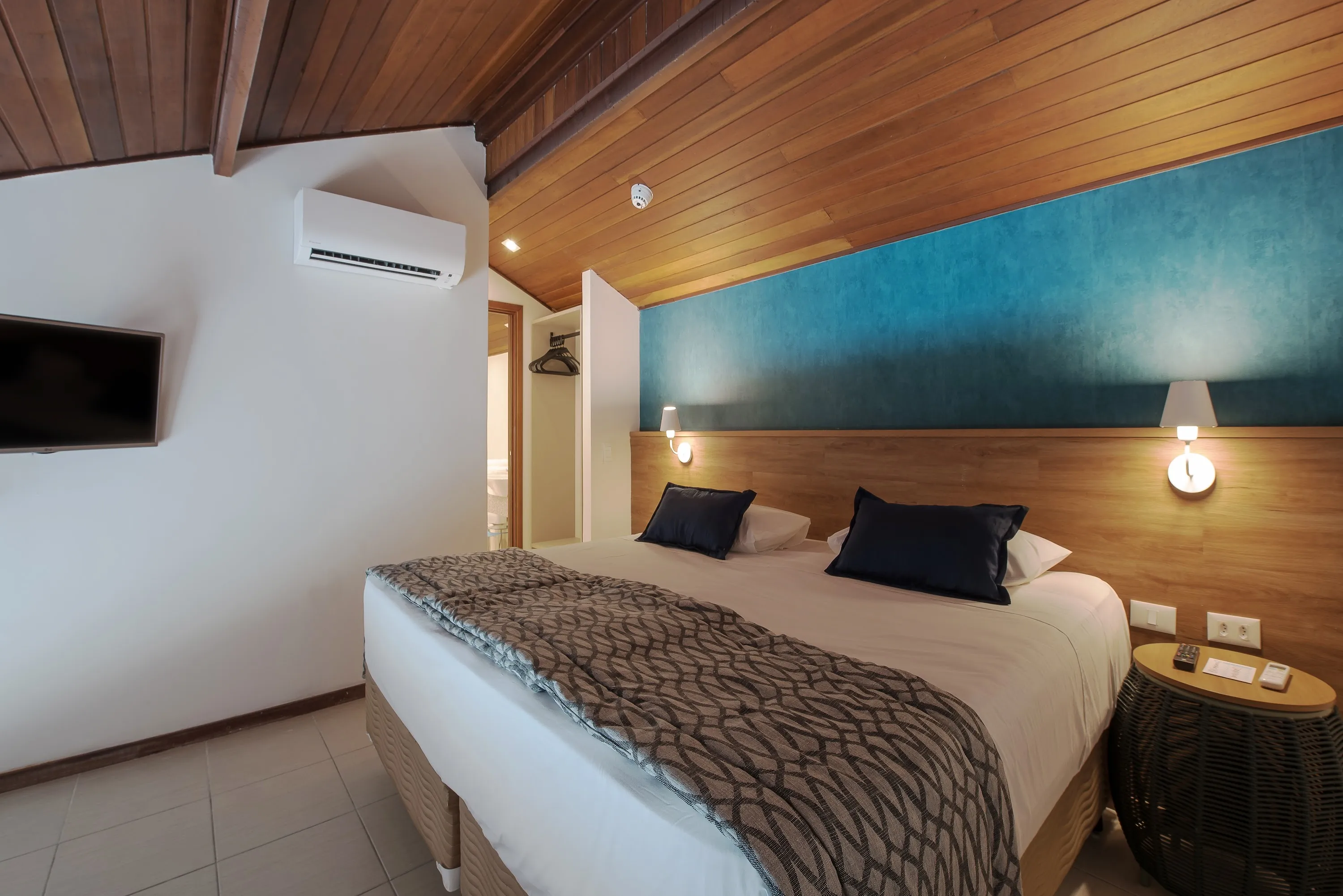 Dos camas soltero dispuestas lado a lado como una cama doble, con luminarias, una para cada lado de la cama, en frente a Tv por cable y aire-condicionado, al lado del ropero y del baño del primer piso.