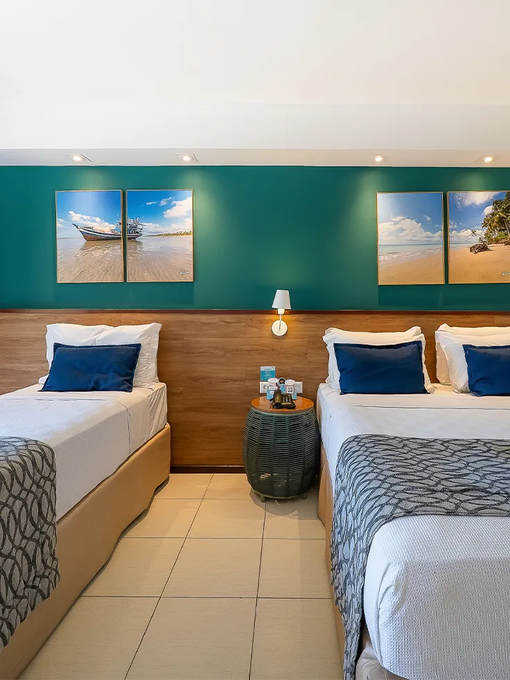 Quarto Apartamento Standard no Salinas Maceió com cama casal e cama solteiro, decoração praiana com parede verde e quadros pendurados na parede, e espaço confortável pra família.