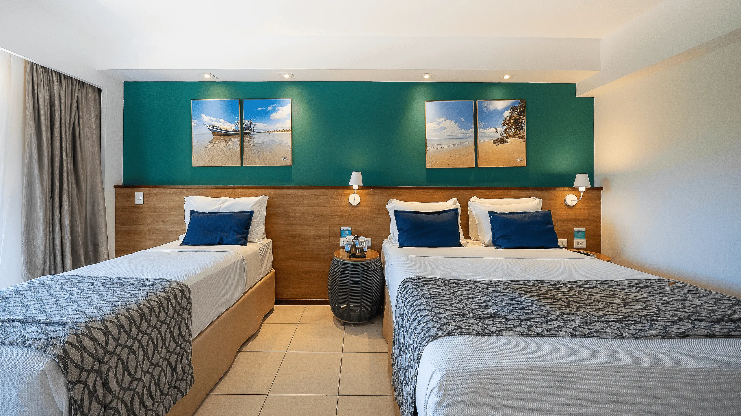 Quarto Apartamento Standard no Salinas Maceió com cama casal e cama solteiro, decoração praiana com parede verde e quadros pendurados na parede, e espaço confortável pra família.