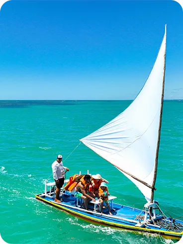 Barquinho a vela colorido navegando com o marinheiro em águas turquesa com céu azul com uma família sorrindo a bordo.