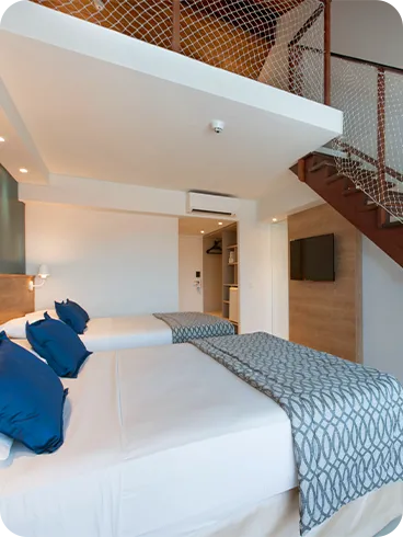 Two single beds arranged side by side like a double bed, with two lamps, one for each side of the bed, in front of the cable TV and air conditioning, next to the closet and bathroom on the upper floor.