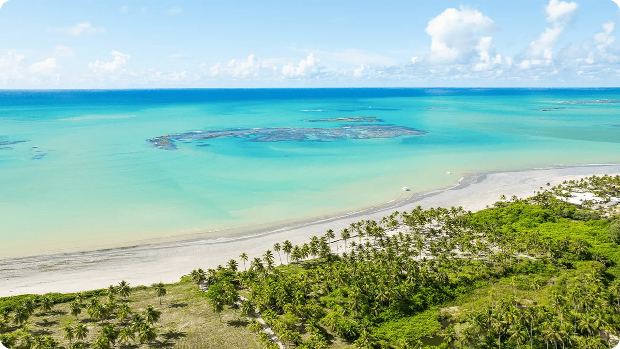 Vista aérea da praia de Ipioca com mar azul-turquesa, recifes de corais, barcos e vegetação tropical bem verde.