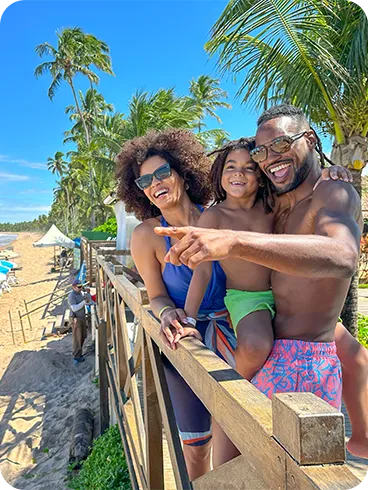 Família sorridente aproveitando dia de sol na praia com cadeiras e guarda-sóis azuis e brancos