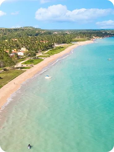 Vista aérea da Praia de Burgalhau com mar turquesa, faixa de areia clara, barcos espalhados, vegetação tropical e morros ao fundo