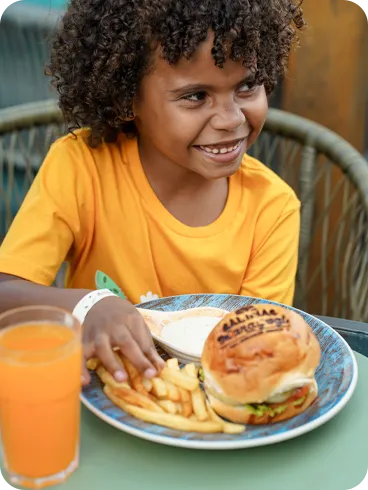 Criança sorridente aproveitando hambúrguer, batata frita e suco durante as férias all inclusive