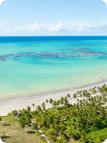 Vista aérea da praia de Ipioca com mar azul-turquesa, recifes de corais, barcos e vegetação tropical bem verde.