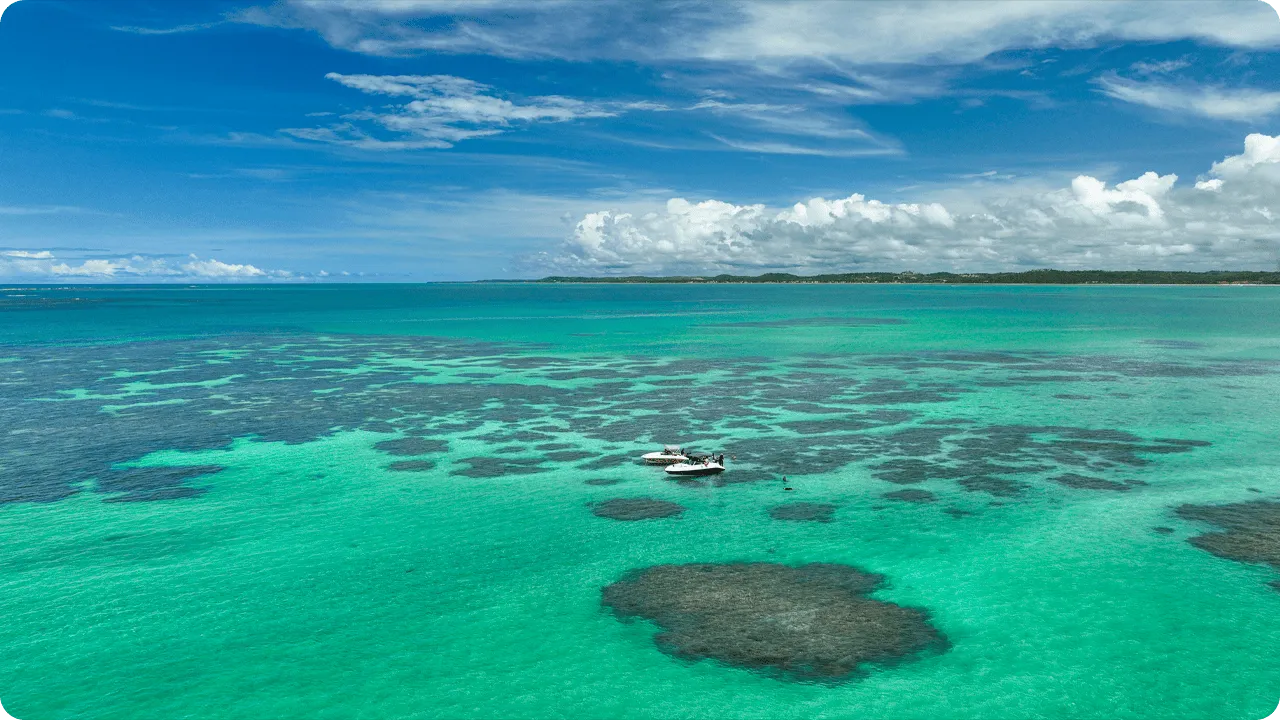 Vista aérea de las piscinas naturales de Maragogi, que muestra vastos arrecifes de coral bajo aguas turquesas cristalinas, con barcos turísticos anclados para que los visitantes practiquen snorkel.