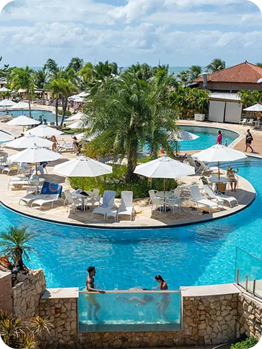 Vista aérea do resort com diversas piscinas e espaços de lazer, perto do mar.