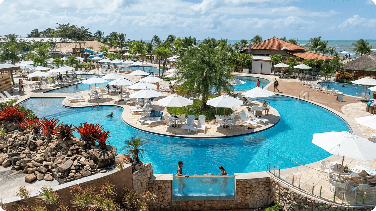 Vista aérea do resort com diversas piscinas e espaços de lazer, perto do mar.