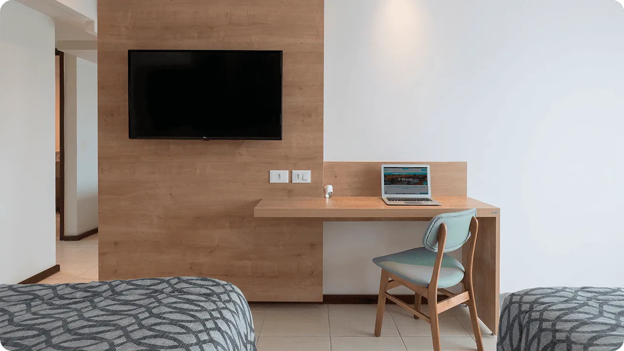 Wooden panel in front of the beds, with cable TV, a table, chair, and mirror next to it.