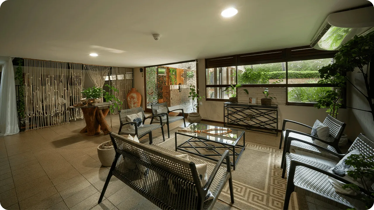 Spa waiting room with comfortable armchairs, decoration with natural plants, soft lighting and a cozy atmosphere overlooking the landscaped outdoor area.