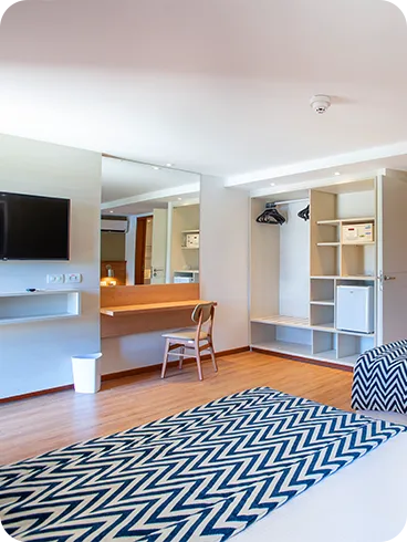 Una cama queen size y una cama individual en la Suite Familia, frente a una mesa y una silla, panel con TV por cable, armario, minibar, caja fuerte digital y baño.