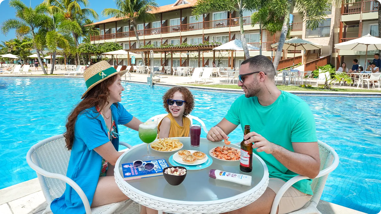 Família se divertindo na área da piscina, com drinks, petiscos e clima ensolarado