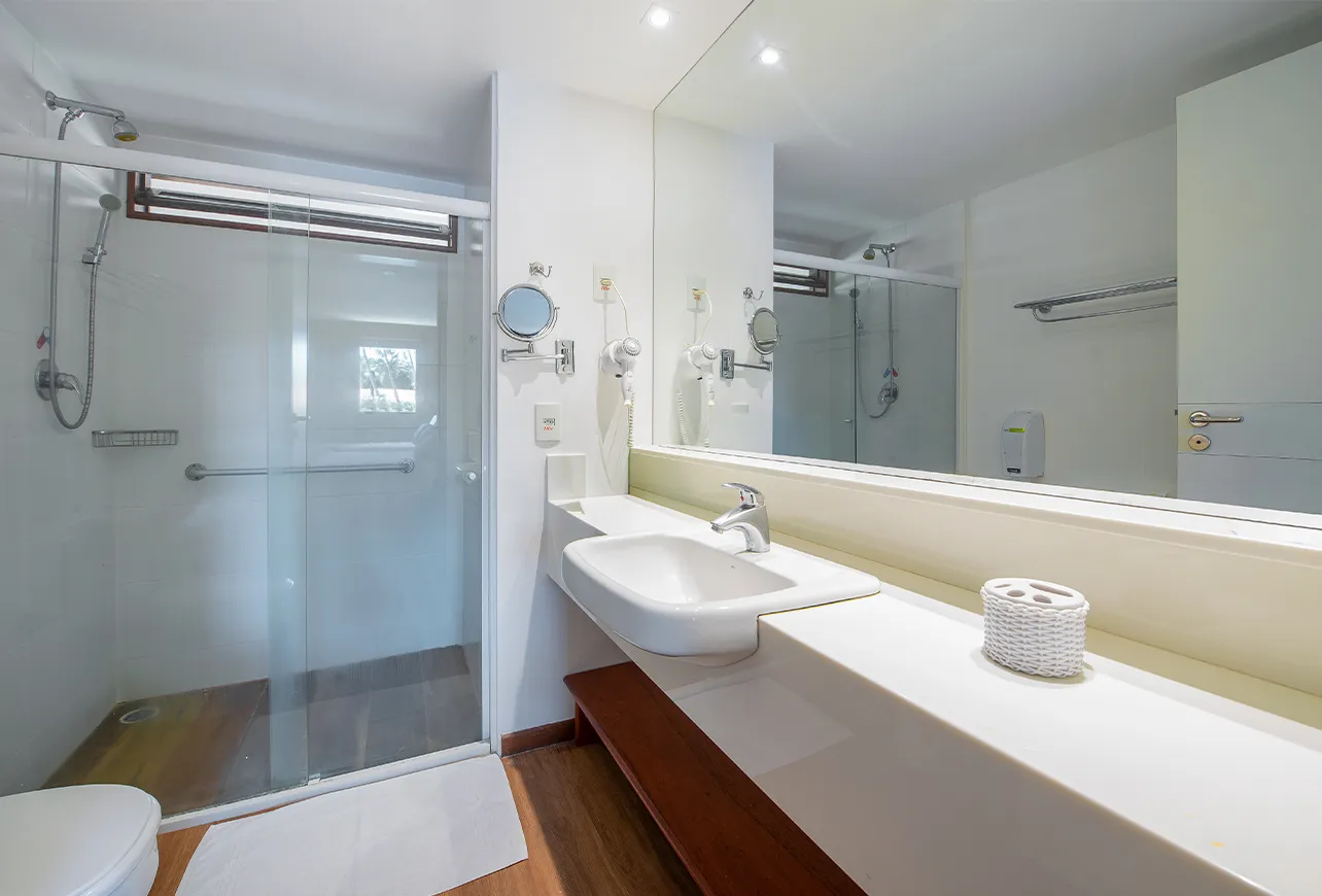 Banheiro da acomodação Standard, contendo área pra banho, instalações sanitárias, chuveiro com regulação de temperatura, decoração, grande espelho e secador de cabelo.