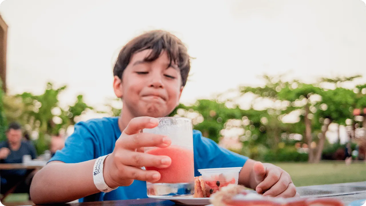 Menino sorridente segurando suco natural e aproveitando sobremesas durante o lanche no resort
