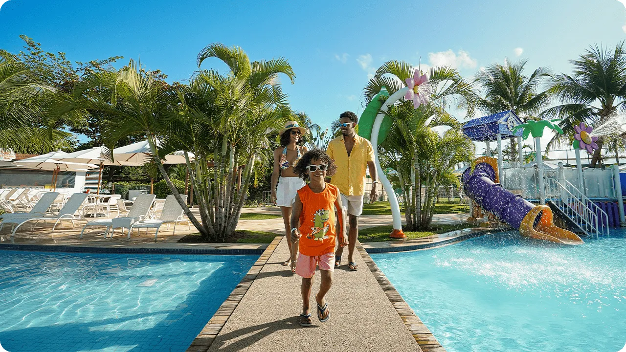 Família caminhando sorridente em área de piscinas e toboáguas de resort