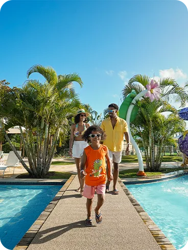 Família caminhando sorridente em área de piscinas e toboáguas de resort