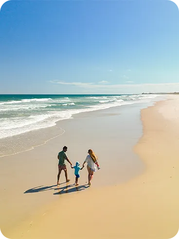 Grande faixa de areia clara da Praia do Francês com uma família caminhando de mãos dadas com mar azul-esverdeado ao fundo e linha de coqueiros à direita.