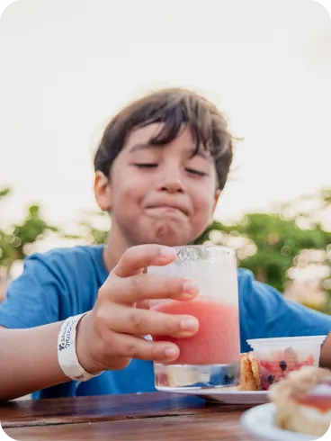 Menino sorridente segurando suco natural e aproveitando sobremesas durante o lanche no resort