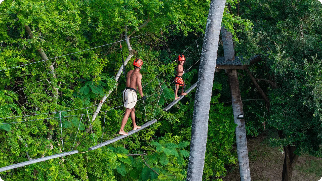 Father and son practicing tree climbing on a suspension bridge between trees at Salinas Maragogi All Inclusive Resort.
