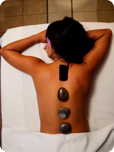 Woman lying on a stretcher receiving hot stone therapy on her back, a relaxation technique used in spas to relieve tension and promote well-being.