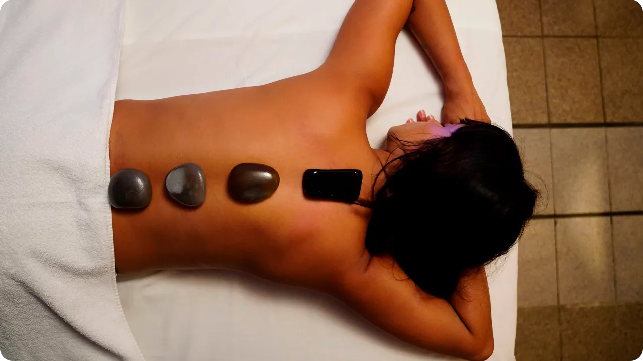 Woman lying on a stretcher receiving hot stone therapy on her back, a relaxation technique used in spas to relieve tension and promote well-being.