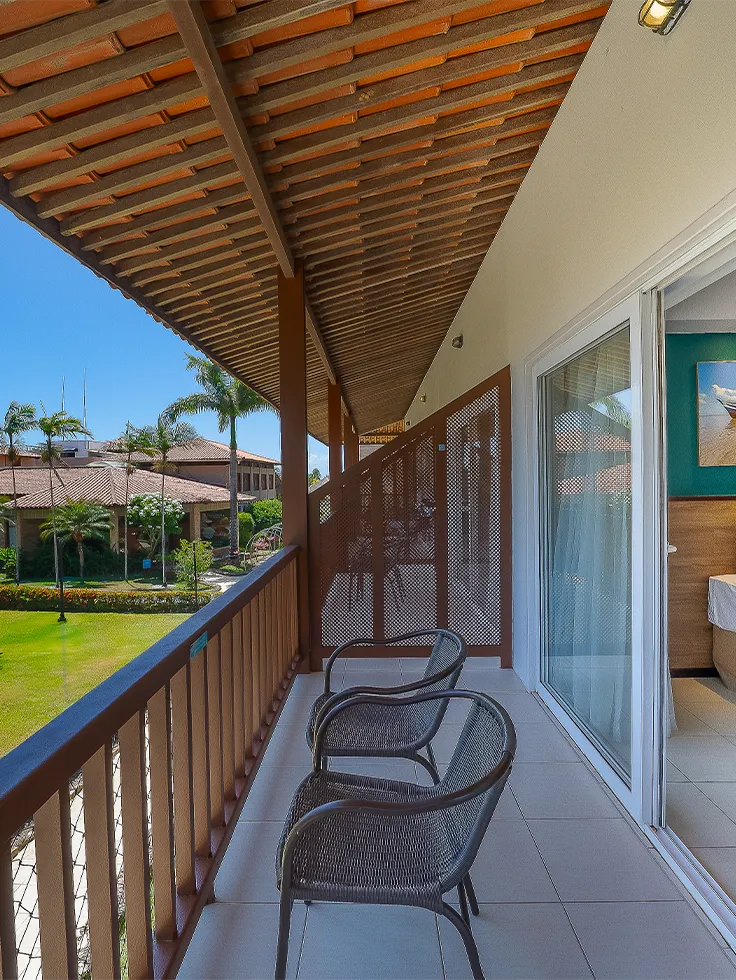 Varanda do Apartamento Standard no Salinas Maceió, ao lado esquerdo a vista pra jardins e área verde do resort e ao lado direito a parte interna do quarto com cama de solteiro.
