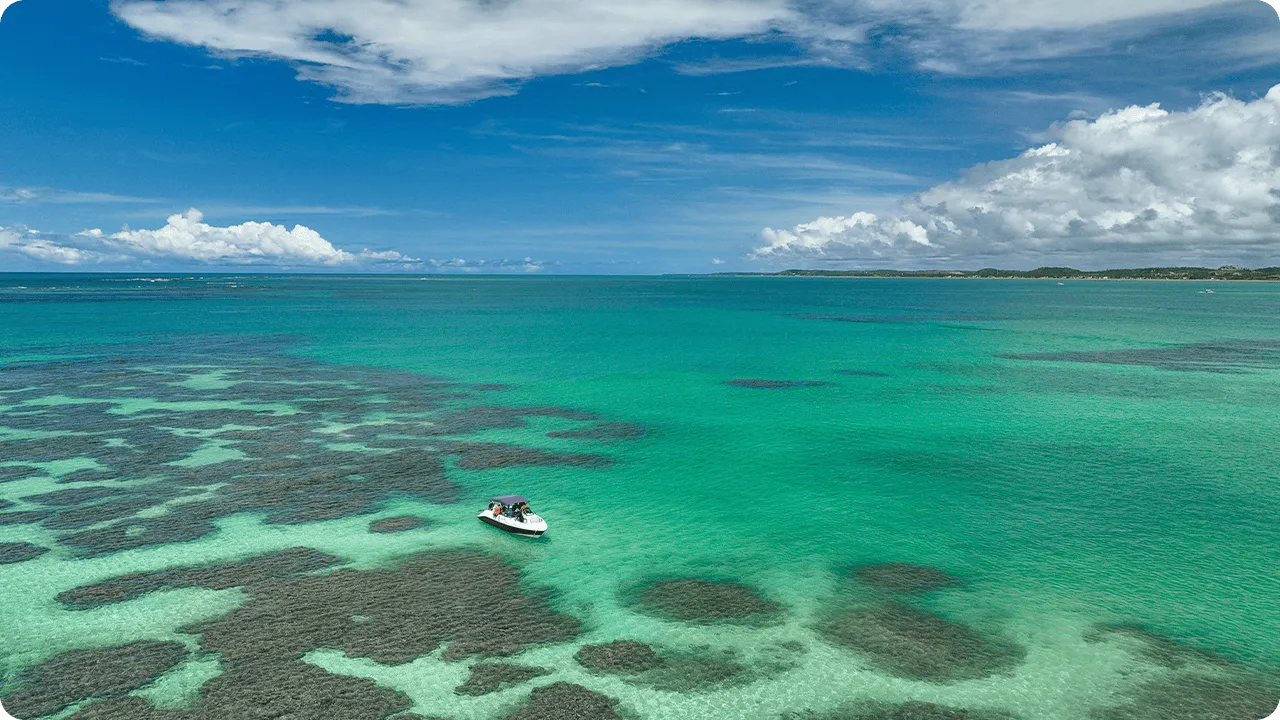 Lancha ancorada sobre as águas cristalinas e rasas das piscinas naturais de Maragogi, com formações de corais visíveis e céu azul, cenário perfeito para passeios de barco no Caribe brasileiro
