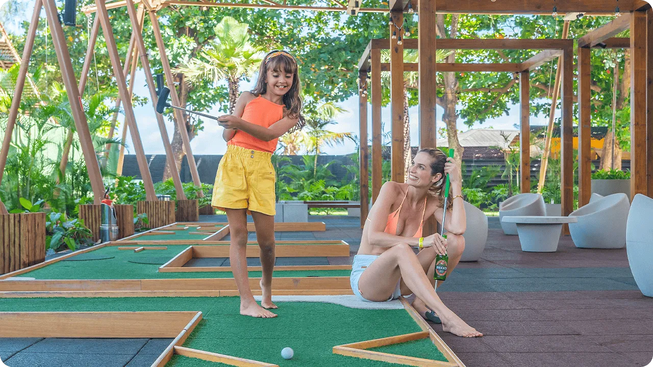 Criança jogando minigolfe ao lado da mãe em área de lazer coberta no resort