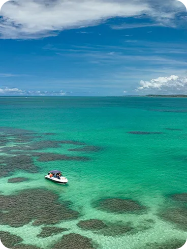 Lancha ancorada sobre as águas cristalinas e rasas das piscinas naturais de Maragogi, com formações de corais visíveis e céu azul, cenário perfeito para passeios de barco no Caribe brasileiro