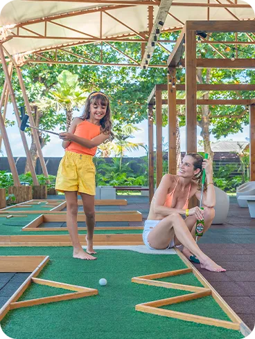 Criança jogando minigolfe ao lado da mãe em área de lazer coberta no resort