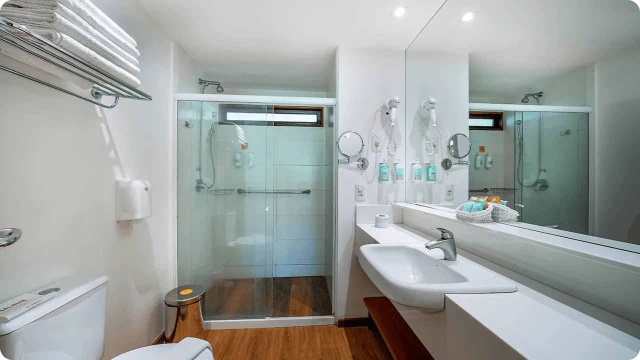 Baño de la Suite Familia, con zona de baño, sanitarios, ducha con control de temperatura, decoración, artículos de aseo O Boticário, toallas, espejo grande y secador de pelo.