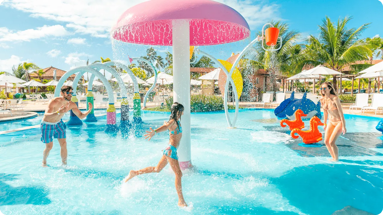 Criança se divertindo com os pais na piscina infantil com escorregadores e jatos de água coloridos.