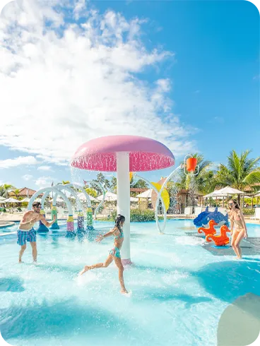 Criança se divertindo com os pais na piscina infantil com escorregadores e jatos de água coloridos.