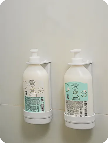 O Boticário shampoo and conditioner, from the Cuide-se Bem line, in refill bottles installed in dispensers on the bathroom's tiled wall.