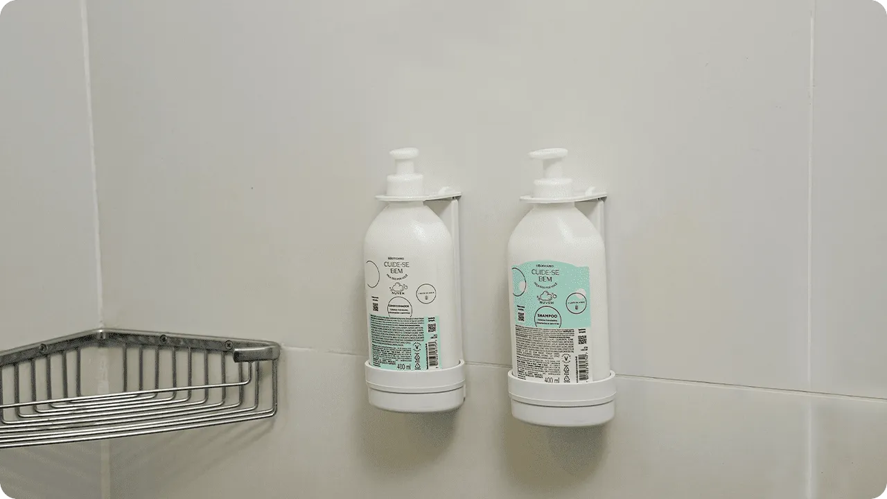 O Boticário shampoo and conditioner, from the Cuide-se Bem line, in refill bottles installed in dispensers on the bathroom's tiled wall.