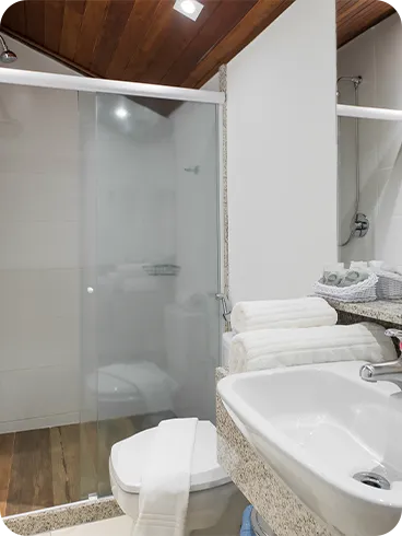 Family Suite bathroom with wooden ceiling, granite countertop, white sink, glass-doored shower and organized white towels.