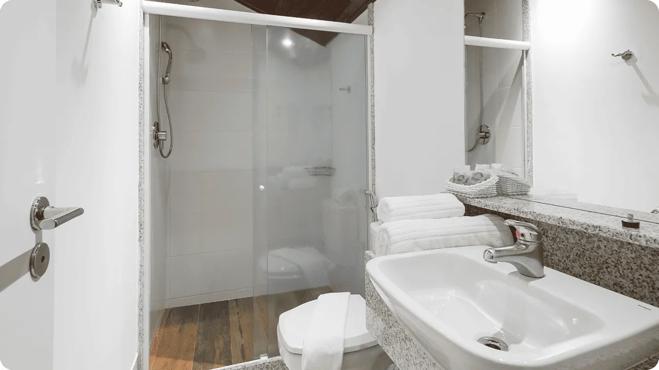 Family Suite bathroom with wooden ceiling, granite countertop, white sink, glass-doored shower and organized white towels.