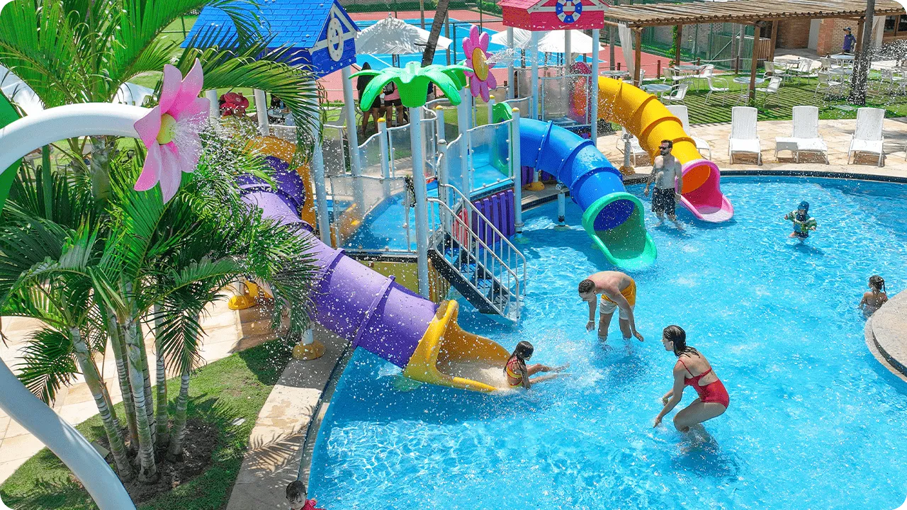 Crianças e adultos brincando em piscina com escorregadores coloridos no resort