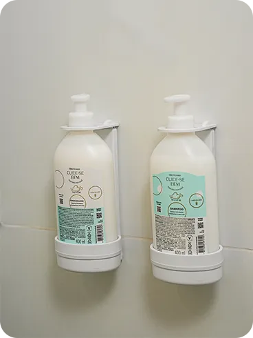 Shampoo e condicionador O Boticário, da linha Cuide-se Bem, em frascos de refil instalados em dispensers na parede de azulejos do banheiro.