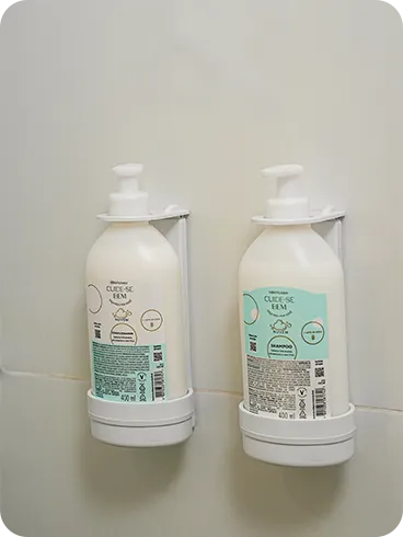 O Boticário shampoo and conditioner, from the Cuide-se Bem line, in refill bottles installed in dispensers on the bathroom's tiled wall.