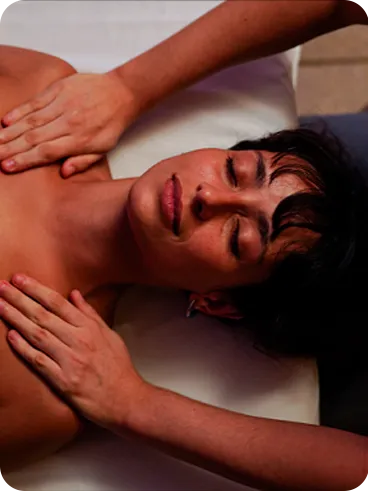 A woman lying on a table in a cozy spa room, receiving a shoulder massage.